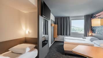 Et hotelværelse med to senge, et lille bord, et spejl og et vindue med gardiner.