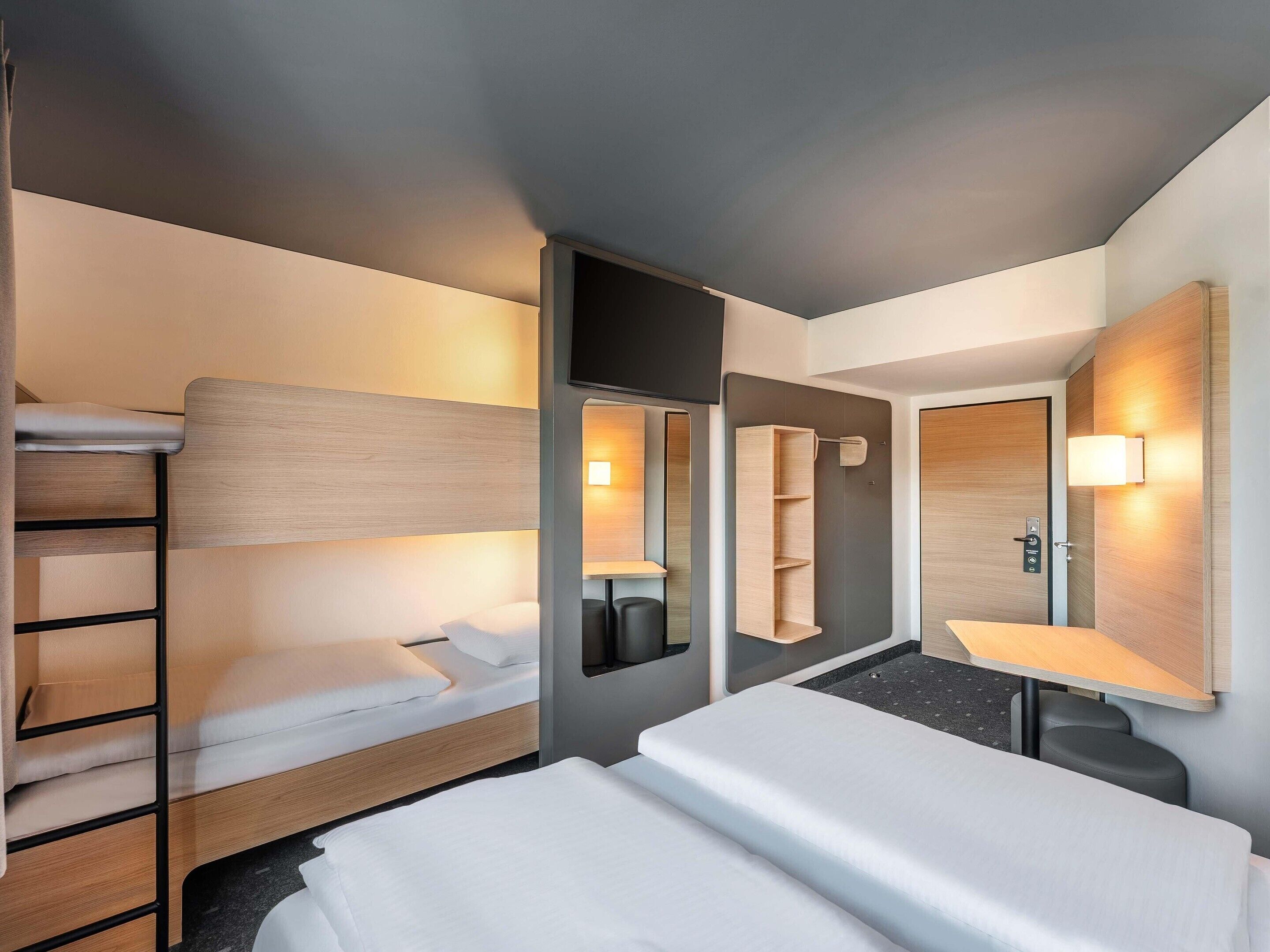 Habitación de hotel con literas, una cama individual, un espejo, una mesita de noche y un estante en la pared.