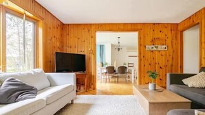 Un salon avec un canapé blanc, un canapé gris, un téléviseur et un coin repas en bois.