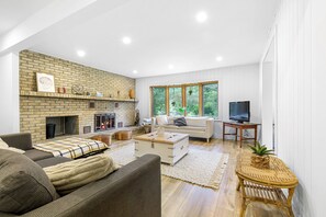 A spacious living room with a fireplace, a television, and a large window offering a view of greenery. - The Horseshoe (Huberdeau)