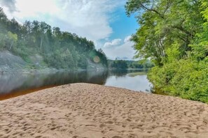 A sandy beach with a calm lake and dense forest in the background. - Le Fer à Cheval 20 min from Tremblant (Huberdeau)