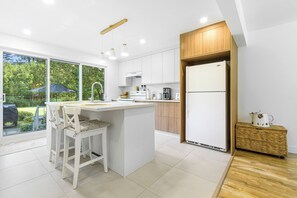 A modern kitchen with a central island, white cabinetry, and a large window overlooking a garden. - The Horseshoe (Huberdeau)