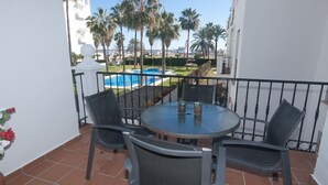 Ein Balkon mit rundem Tisch und Stühlen mit Blick auf einen Swimmingpool und Palmen.