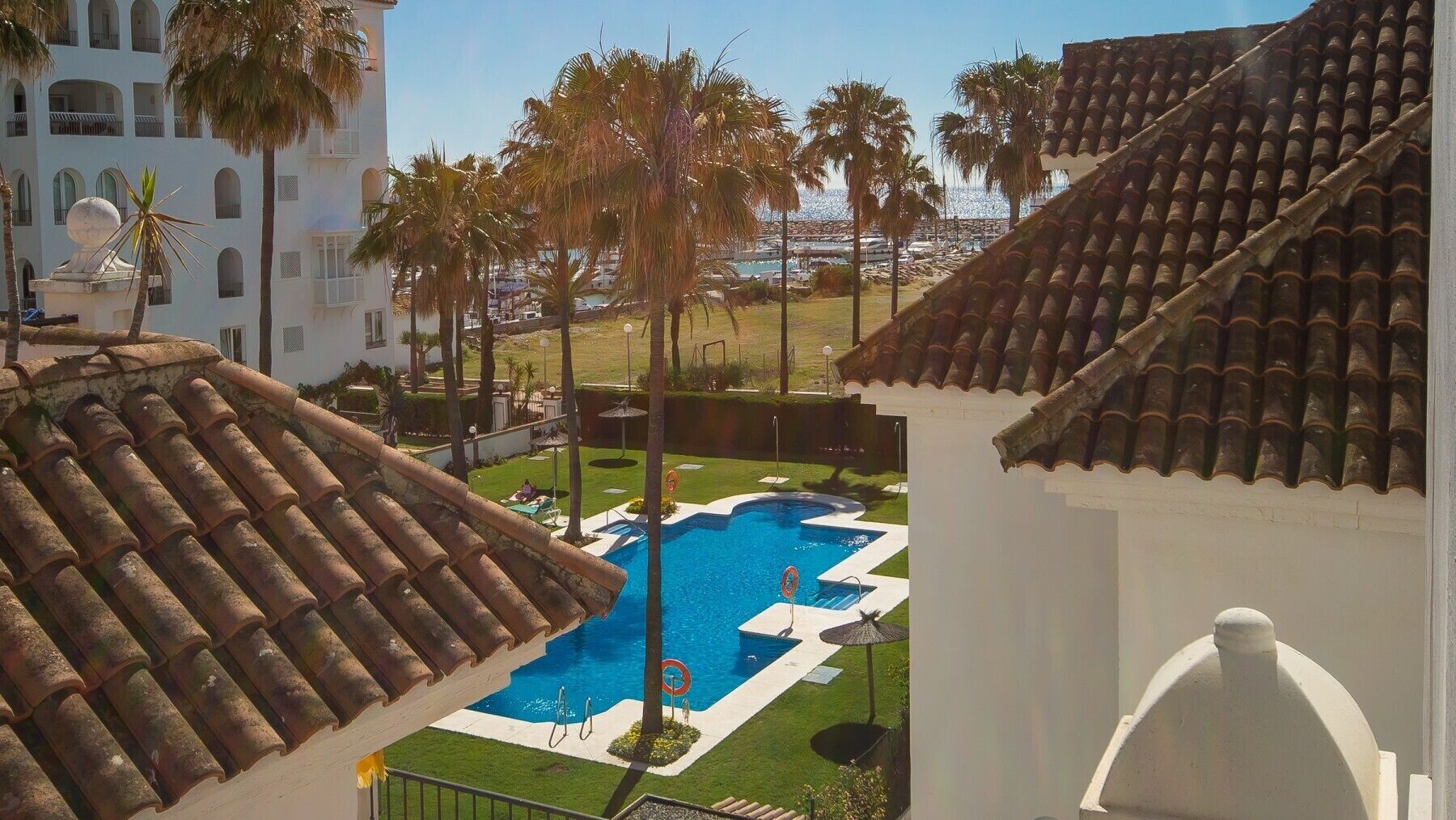 A rooftop pool with a clear view of the surrounding area, including a building with a white facade and a tiled roof.