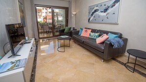 A modern living room with a sofa, coffee table, and a laptop on a desk. There is a balcony with a view of buildings. - Marina del Castillo 302 (Manilva)