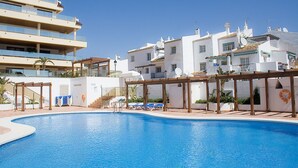 A swimming pool with lounge chairs and a pergola, surrounded by white buildings with balconies and satellite dishes. - Marina del Castillo 302 (Manilva)