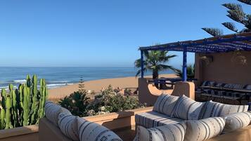 A beachside patio with a view of the ocean, a covered seating area, and cacti.