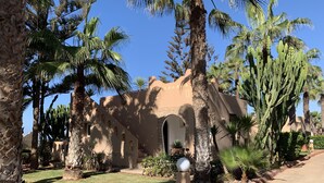 A desert-style building with arched doorways and a stone facade, surrounded by palm trees and cacti.