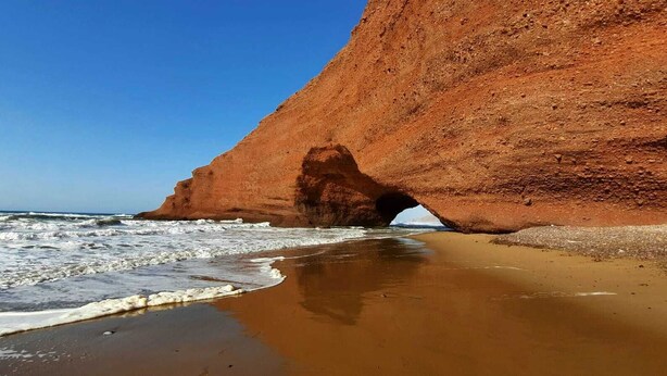 A coastal landscape with a prominent red rock formation and a beach.