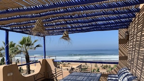 A covered outdoor seating area with a table and chairs, overlooking the beach and ocean.