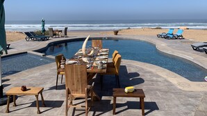 A poolside dining area with a view of the ocean, wooden furniture, and a small table with a decorative item.