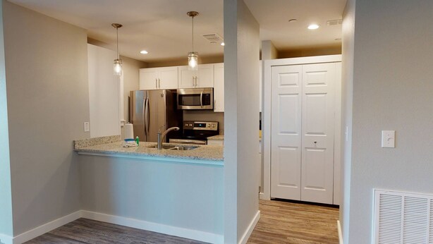 A modern kitchen with stainless steel appliances, a granite countertop, and a white door in the background. - First Floor, Shared Pool, Hot Tub, Pet Friendly, Golf Cart Access (Port Aransas)