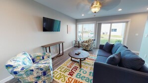 A modern living room with a sofa, a patterned armchair, a coffee table, and a flat-screen TV mounted on the wall. - First Floor, Shared Pool, Hot Tub, Pet Friendly, Golf Cart Access (Port Aransas)