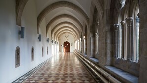 Un long couloir au sol à carreaux, doté de voûtes et de colonnes en pierre.