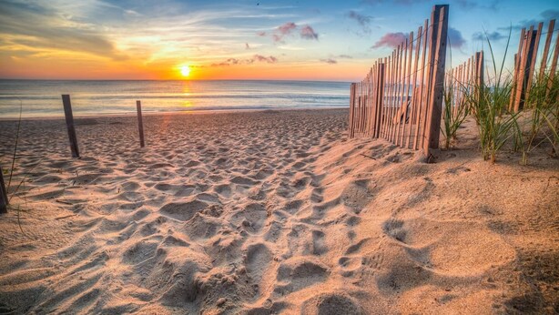 A sandy beach with wooden fencing and a sunset in the background. - The East Coast Host - Back To Eden (Kill Devil Hills NC)