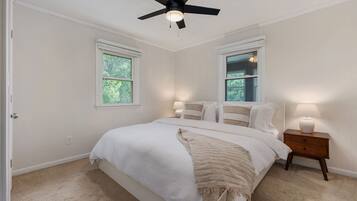 A bedroom with a bed, two bedside lamps, a ceiling fan, and two windows.
