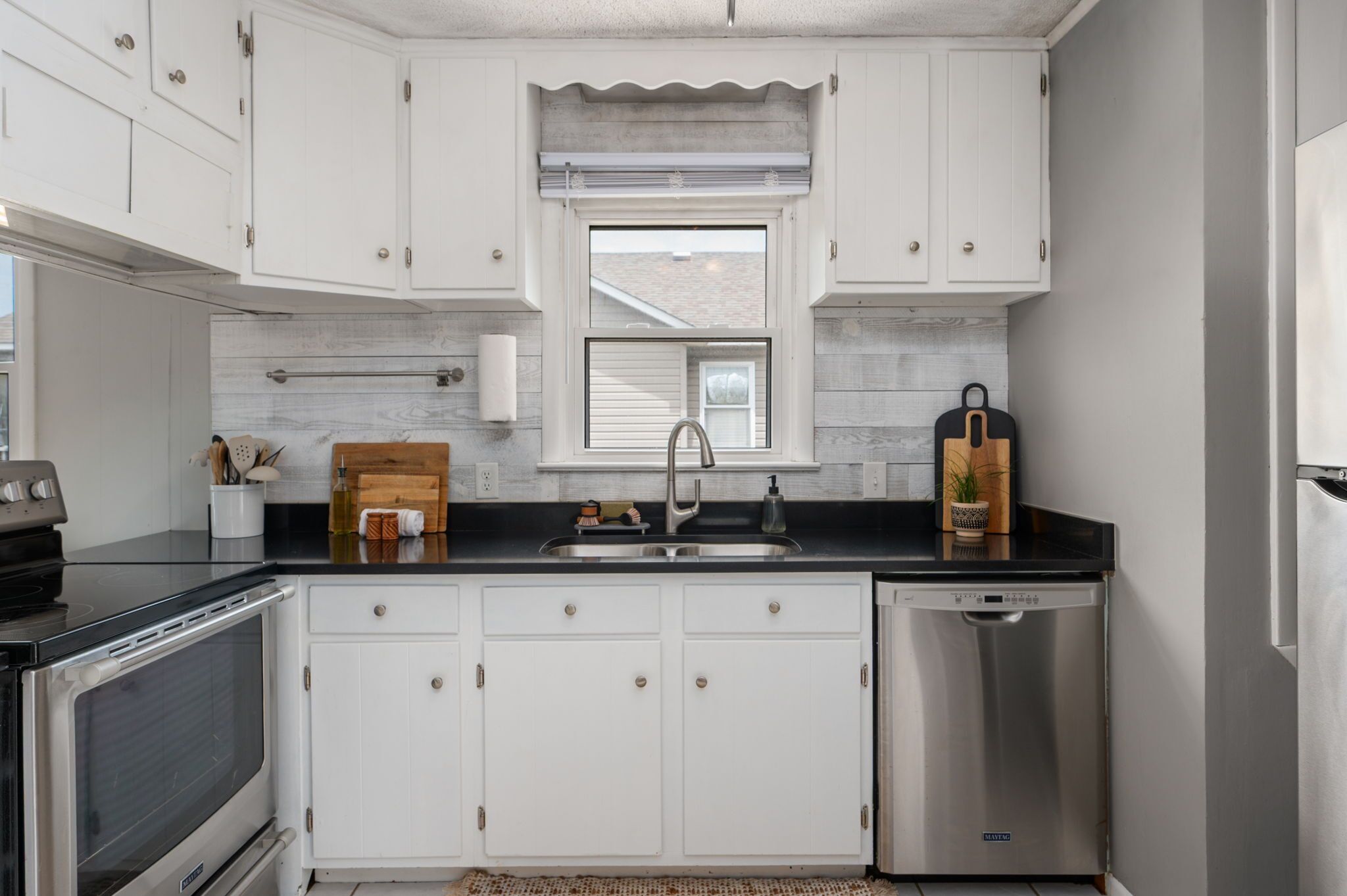 A kitchen with white cabinets, a stainless steel sink, a dishwasher, and a window above the sink.