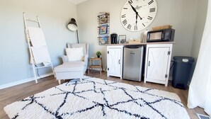 A modern kitchen with white cabinets, a stainless steel refrigerator, a microwave, and a large wall clock.