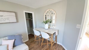 A cozy living room with a white sofa, a small dining table with two chairs, and a mirror above the table.