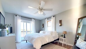A bedroom with a bed, a ceiling fan, a nightstand, a mirror, and a window with curtains.