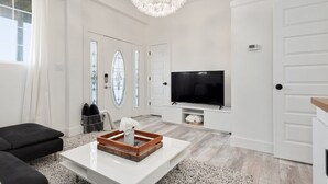 A modern living room with a large flat-screen TV, a white coffee table, and a black sofa.