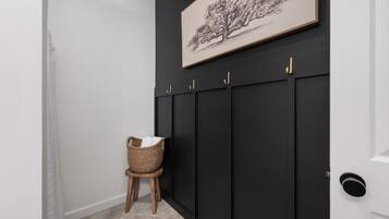 Un pasillo con una pared oscura, una obra de arte con un árbol enmarcado y una cesta de mimbre sobre un taburete.