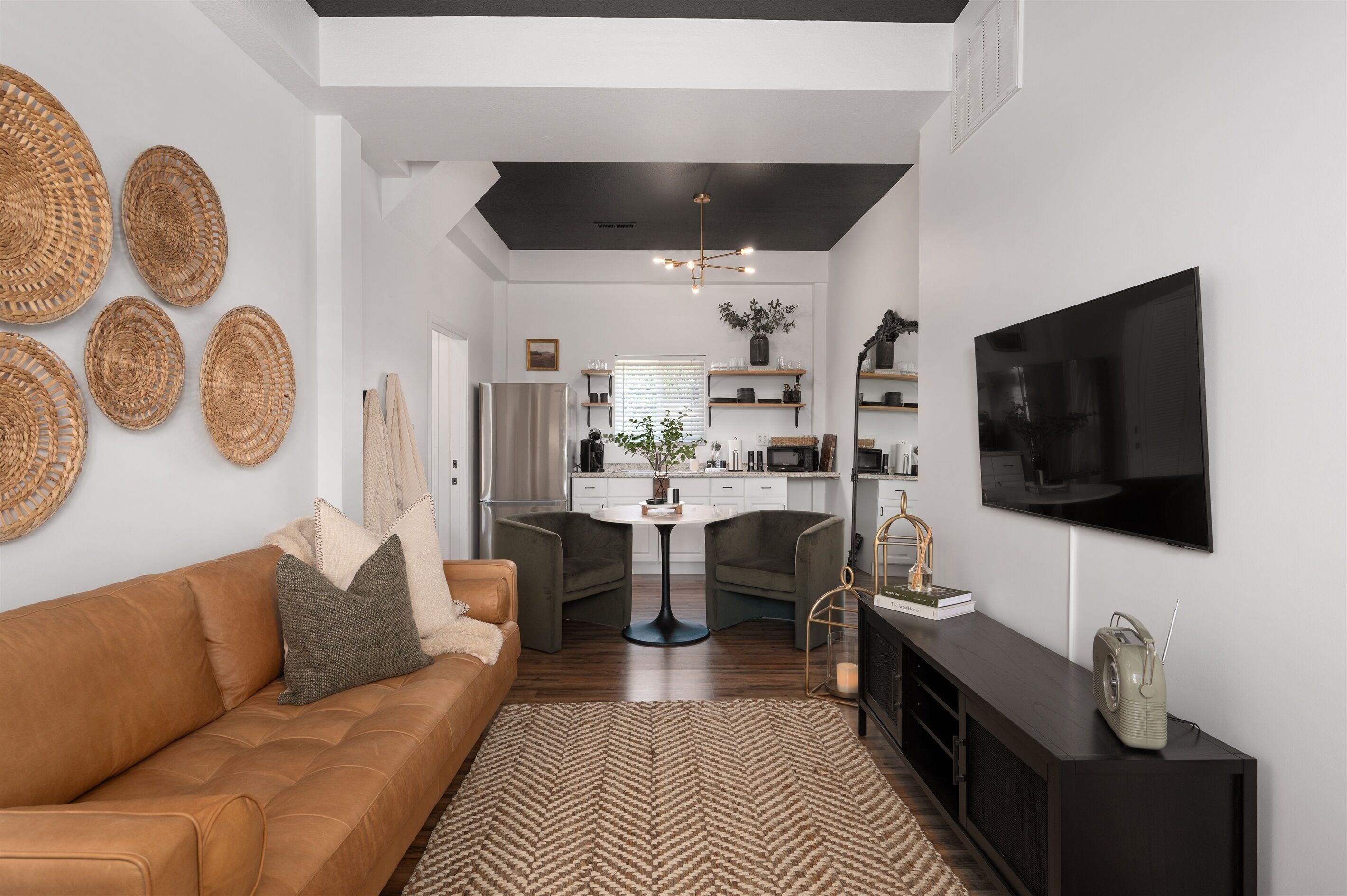 Ein modernes Wohnzimmer mit einem braunen Ledersofa, einem Teppich mit Fischgrätmuster und einem an der Wand montierten Fernseher.