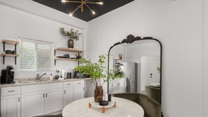 A modern kitchen with white cabinets, a round marble table, and a large mirror.