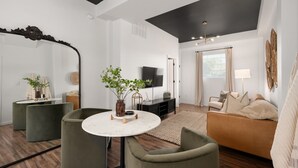 A modern living room with a round table, green armchairs, a sofa, and a TV.