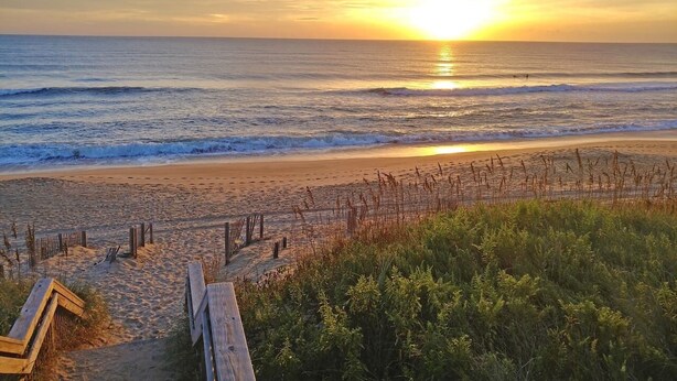 A beach with a wooden walkway leading to the shore, surrounded by vegetation.