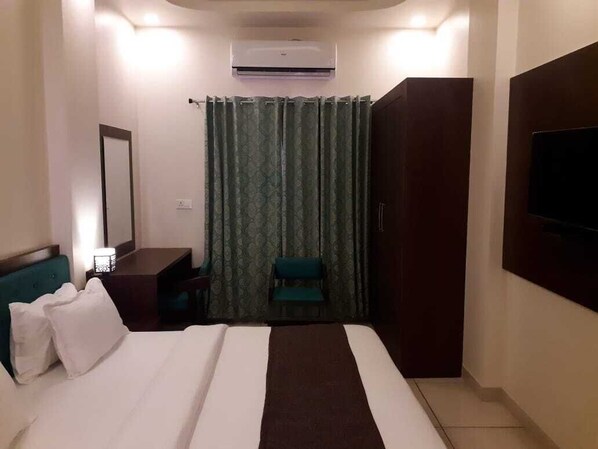 A hotel room with a bed, a desk, a chair, a TV, and an air conditioning unit.