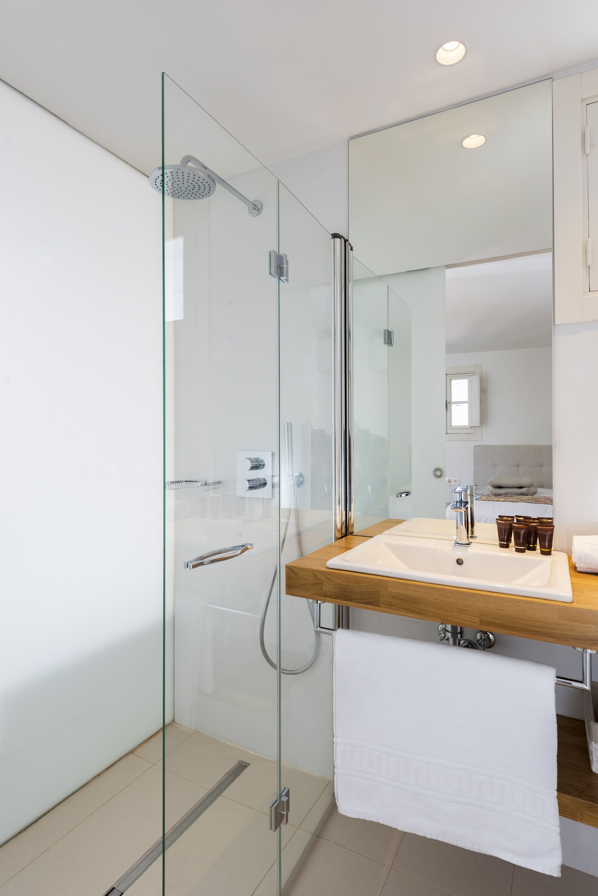 A modern bathroom with a glass shower enclosure, a wooden vanity with a sink, and a large mirror.