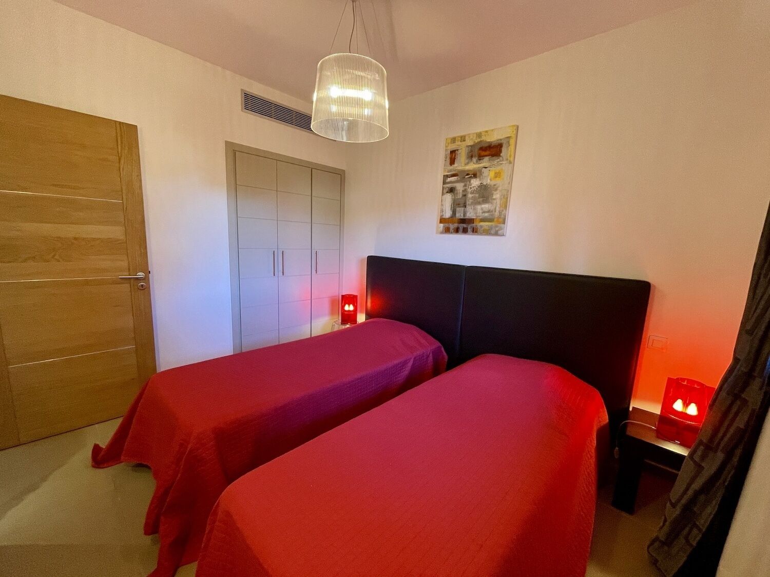 A room with two single beds, a wooden door, a white wardrobe, and a ceiling light.