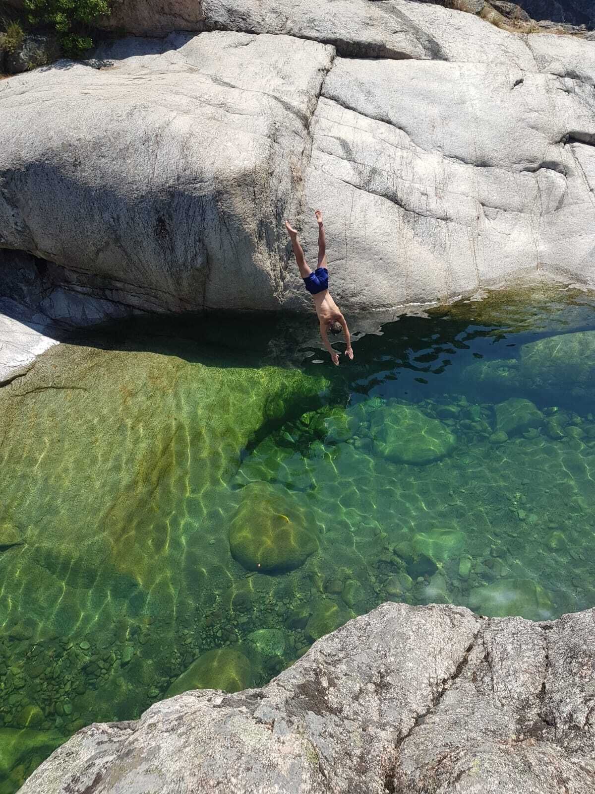 Una persona si tuffa in una piscina cristallina circondata da grosse rocce.