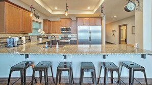 A modern kitchen with granite countertops, stainless steel appliances, and bar stools.