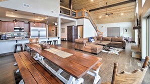A spacious living area with a wooden dining table, a leather sofa, and a staircase leading to an upper level.