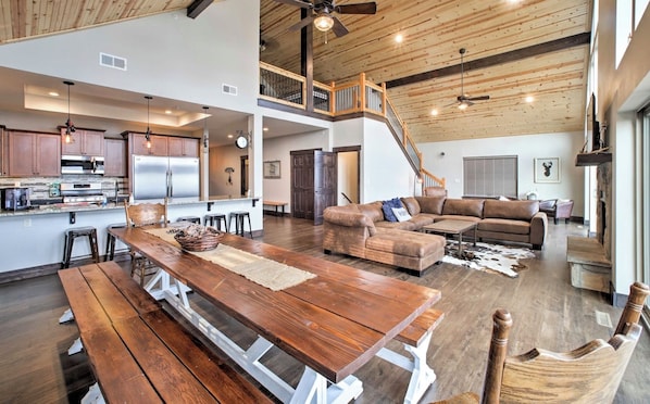 A spacious living area with a wooden dining table, a leather sofa, and a staircase leading to an upper level.