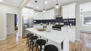 A modern kitchen with white cabinetry, a central island with stools, stainless steel appliances, and pendant lighting.