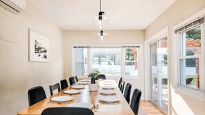 A dining room with a long wooden table, black chairs, and a hanging light fixture.
