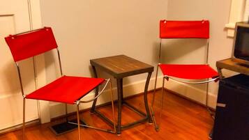 Dos sillas rojas con estructura metálica y una pequeña mesa de madera en una habitación con suelo de madera y paredes blancas.