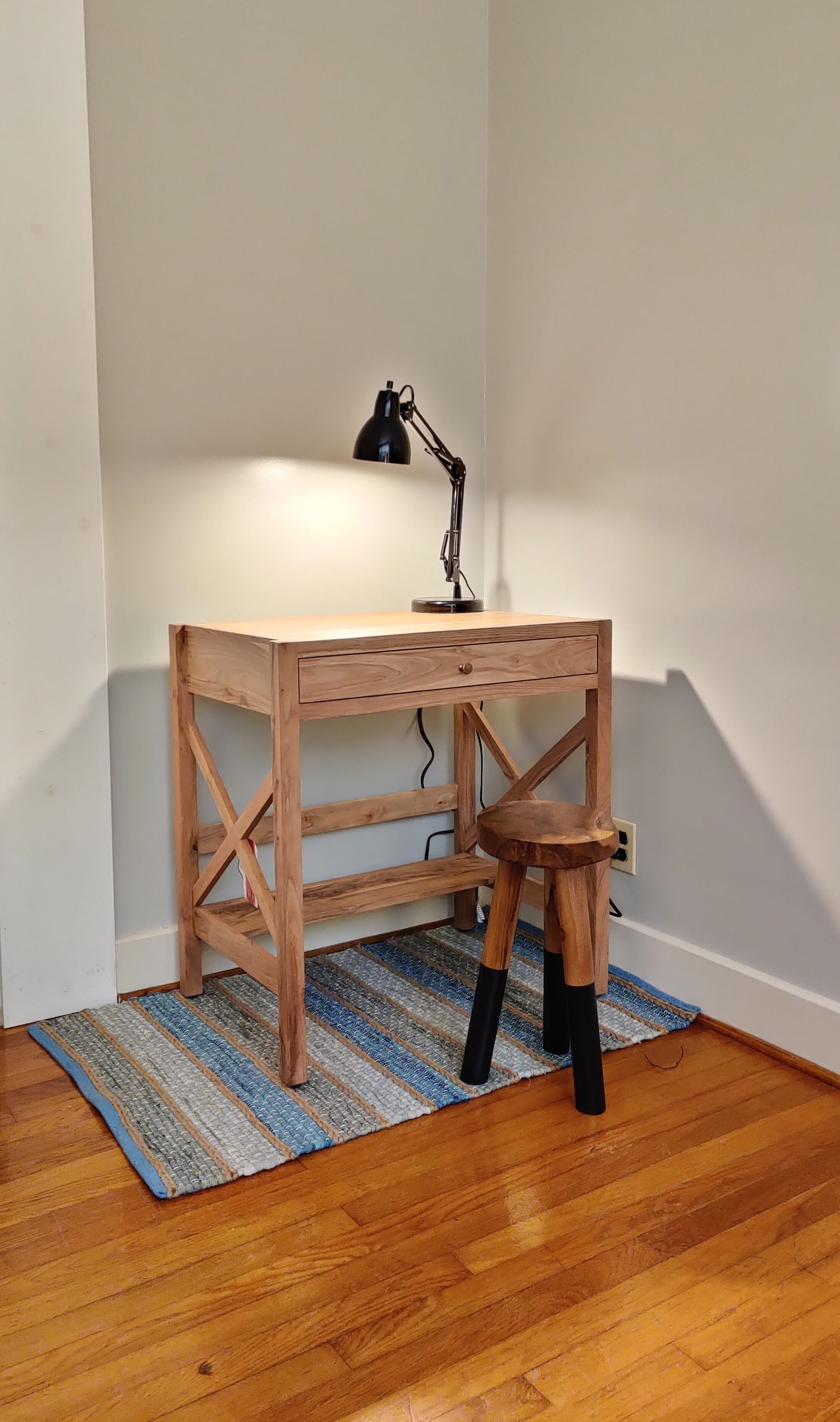 Uma mesa de madeira com uma luminária de mesa preta e um banquinho de madeira.