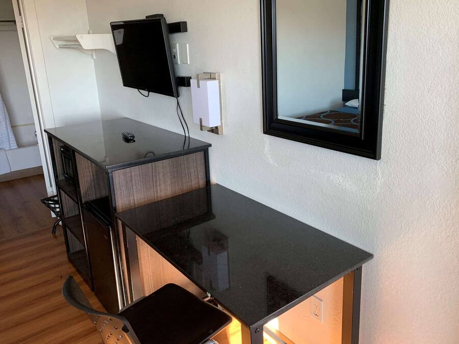 Una habitación compacta y moderna con un escritorio negro elegante, un televisor de pantalla plana montado y un espejo grande.