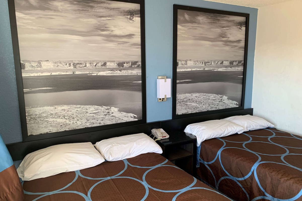 A hotel room with two beds, a large window with a view of a snowy landscape, and a bedside table with a phone.