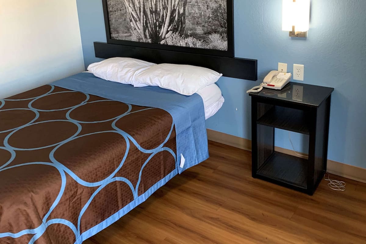A neatly made bed with a patterned bedspread, a bedside table with a phone, and a wall-mounted light fixture.