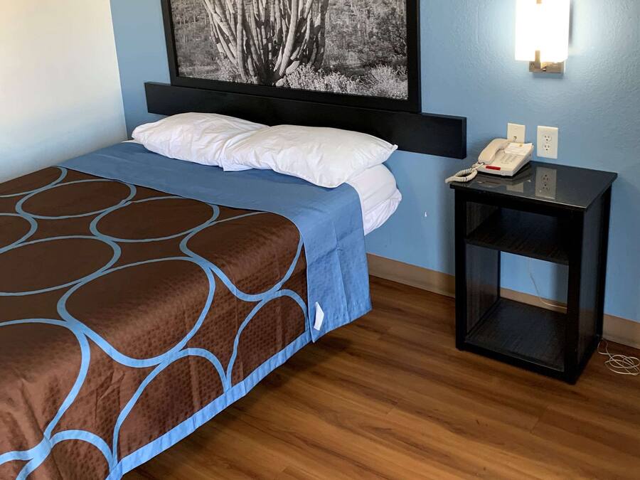 Una cama bien hecha con un edredón estampado, una mesita de noche con un teléfono y una lámpara de pared.
