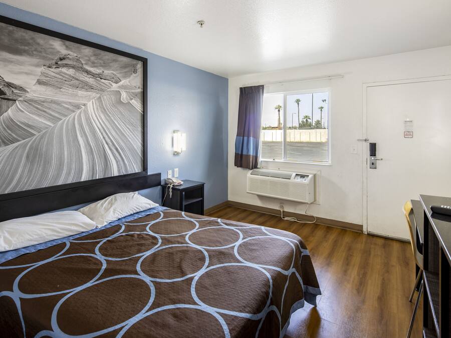 Une chambre d’hôtel avec un grand lit, un bureau, une chaise, une fenêtre avec des rideaux et une porte.