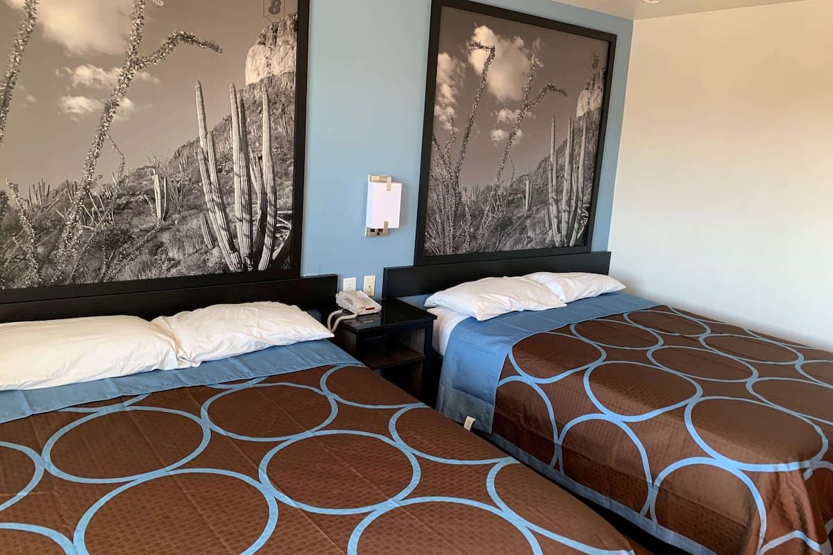A hotel room with two beds, a nightstand, and a wall-mounted phone.