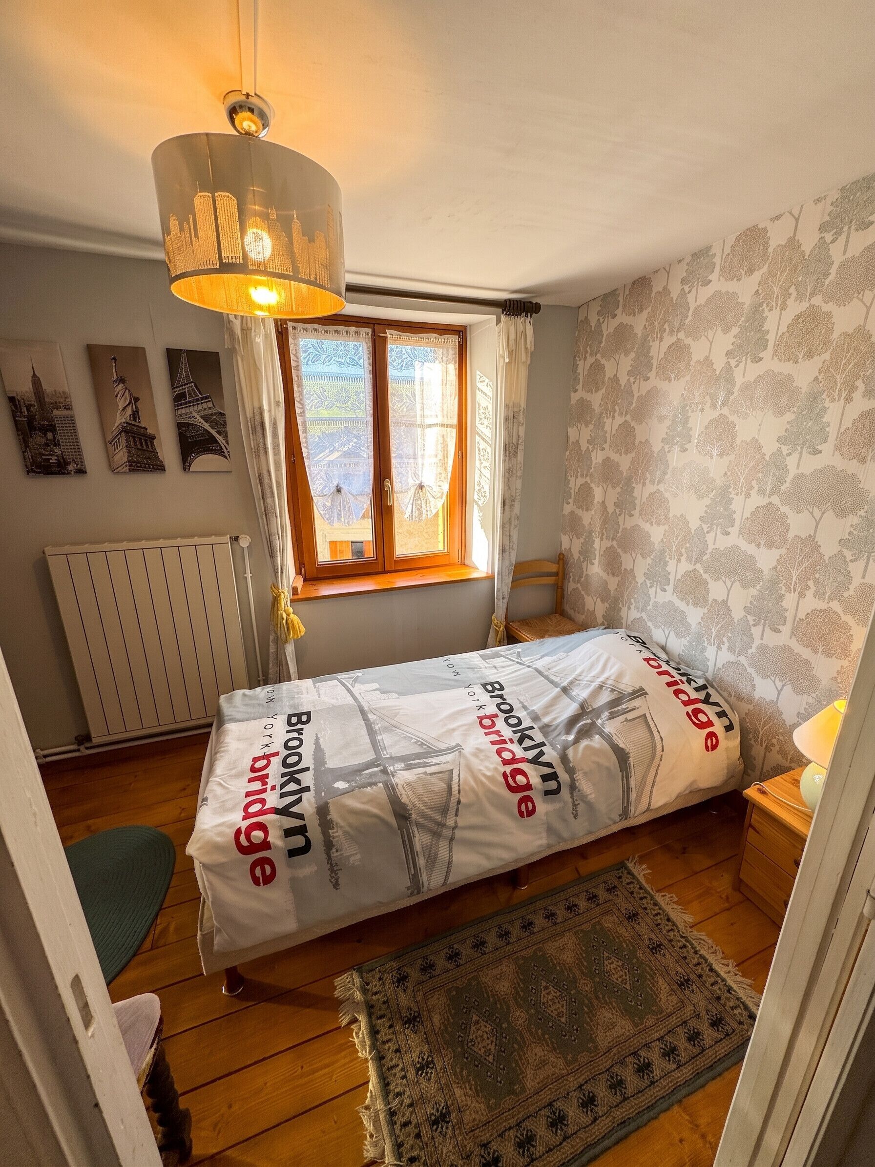 A bedroom with a bed, a window with curtains, a radiator, and wall art.