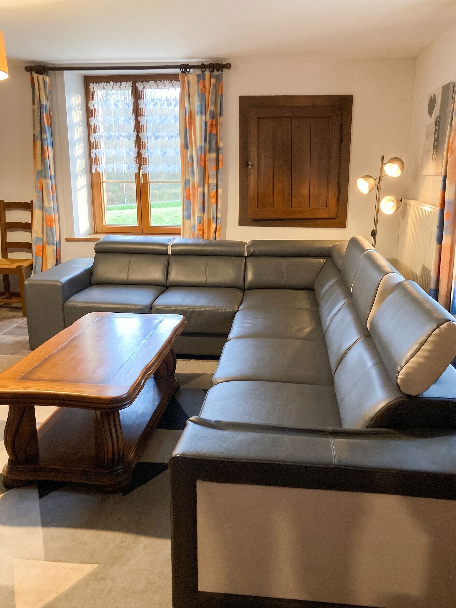 Un salon moderne avec un canapé d’angle, une table basse en bois et une grande fenêtre agrémentée de rideaux.