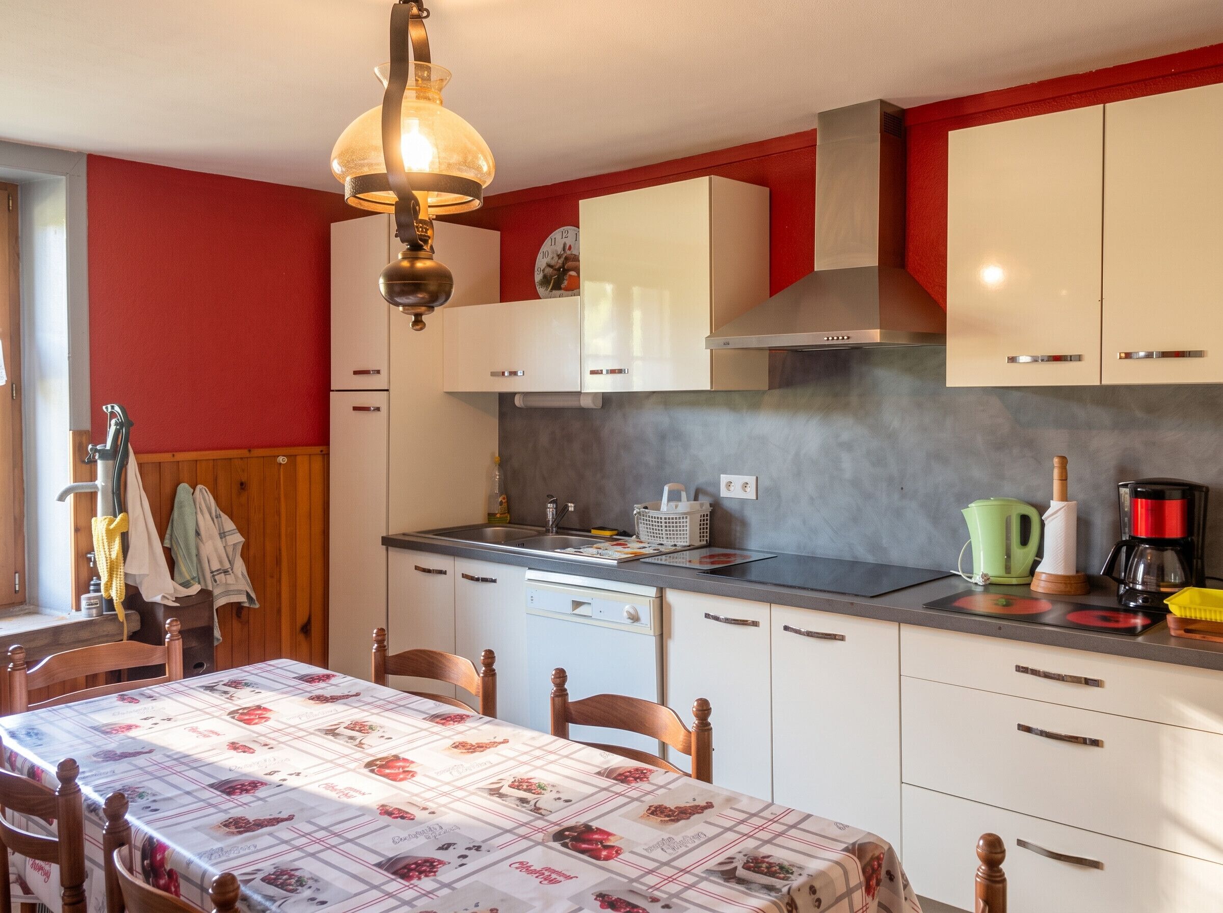 Una cucina con mobili bianchi, un piano di lavoro in acciaio inossidabile, una lampada a sospensione e un tavolo con tovaglia floreale.